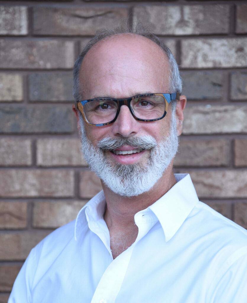 Fred Harvey, MD, smiling, in glasses and a white shirt against a brick wall