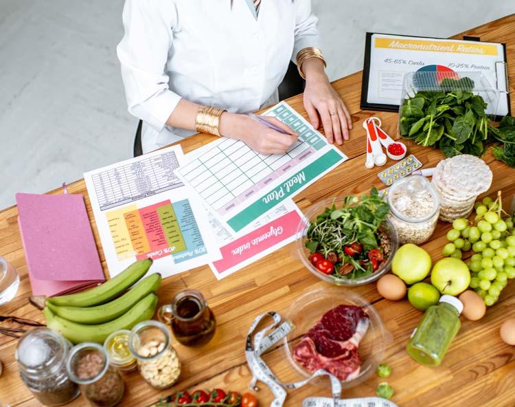 Clinician writing a meal plan at a table set with foods, supplements and a tape measure