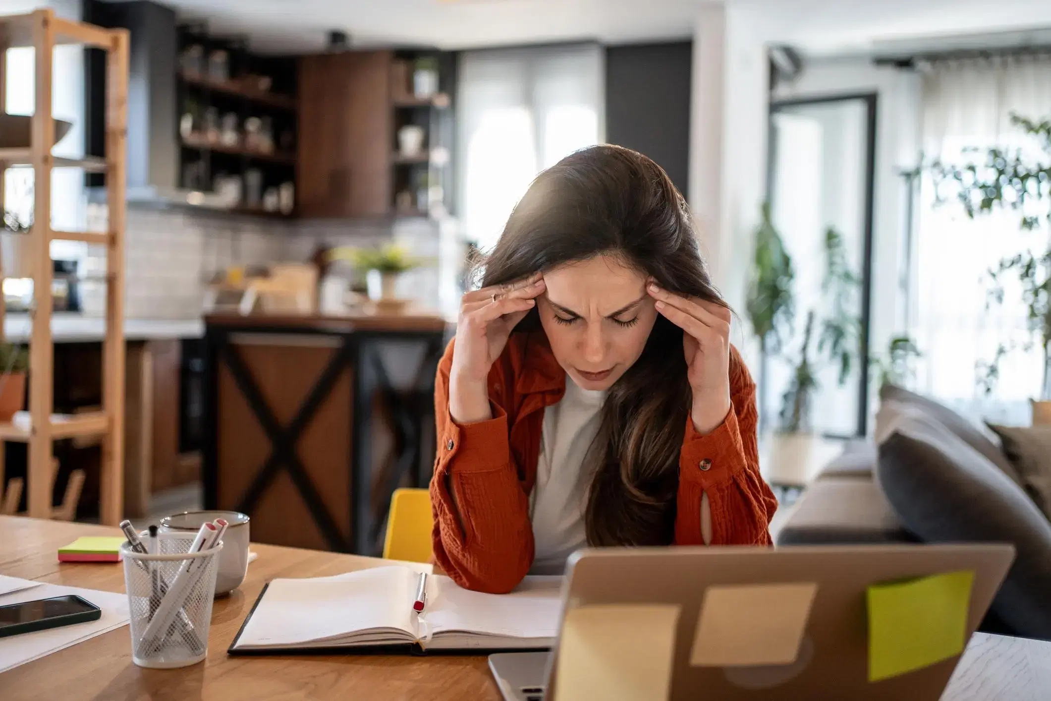 A woman at a table with a laptop, holding her temples with her eyes closed