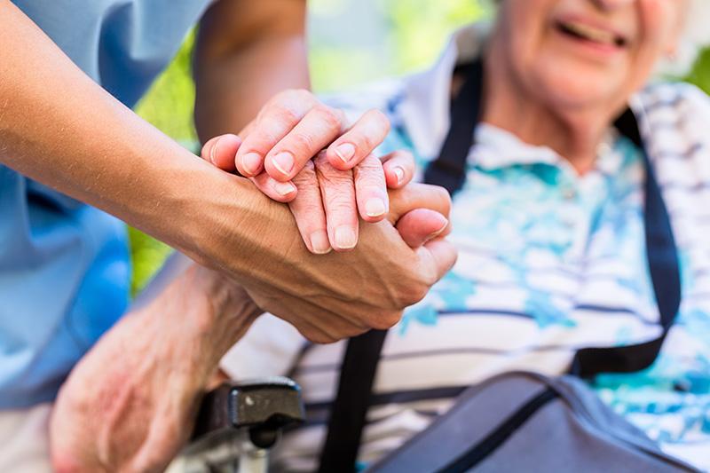 A caregiver's hands clasping an older woman's hand