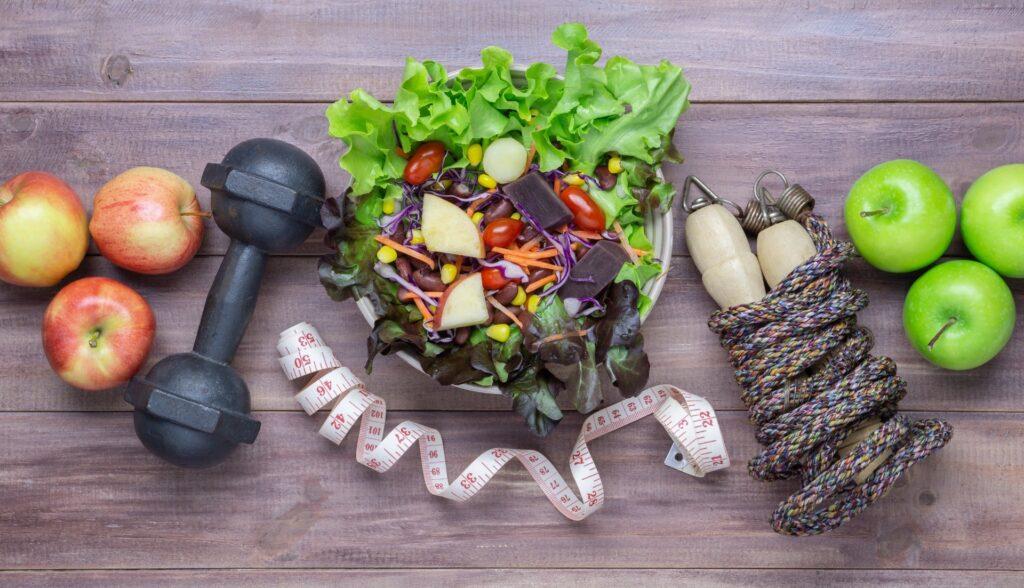 A salad bowl, dumbbell, tape measure, jump rope and apples on a wooden surface