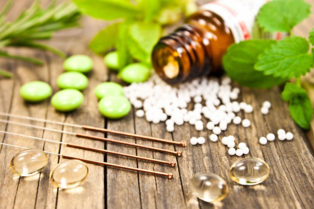 Acupuncture needles, an amber bottle of white pellets, tablets and softgel capsules on a wooden table