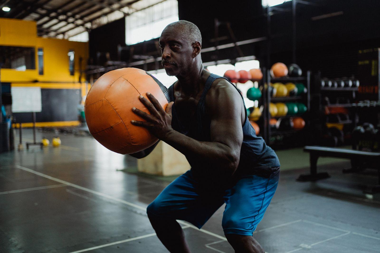 An older man squatting with a medicine ball in a gym